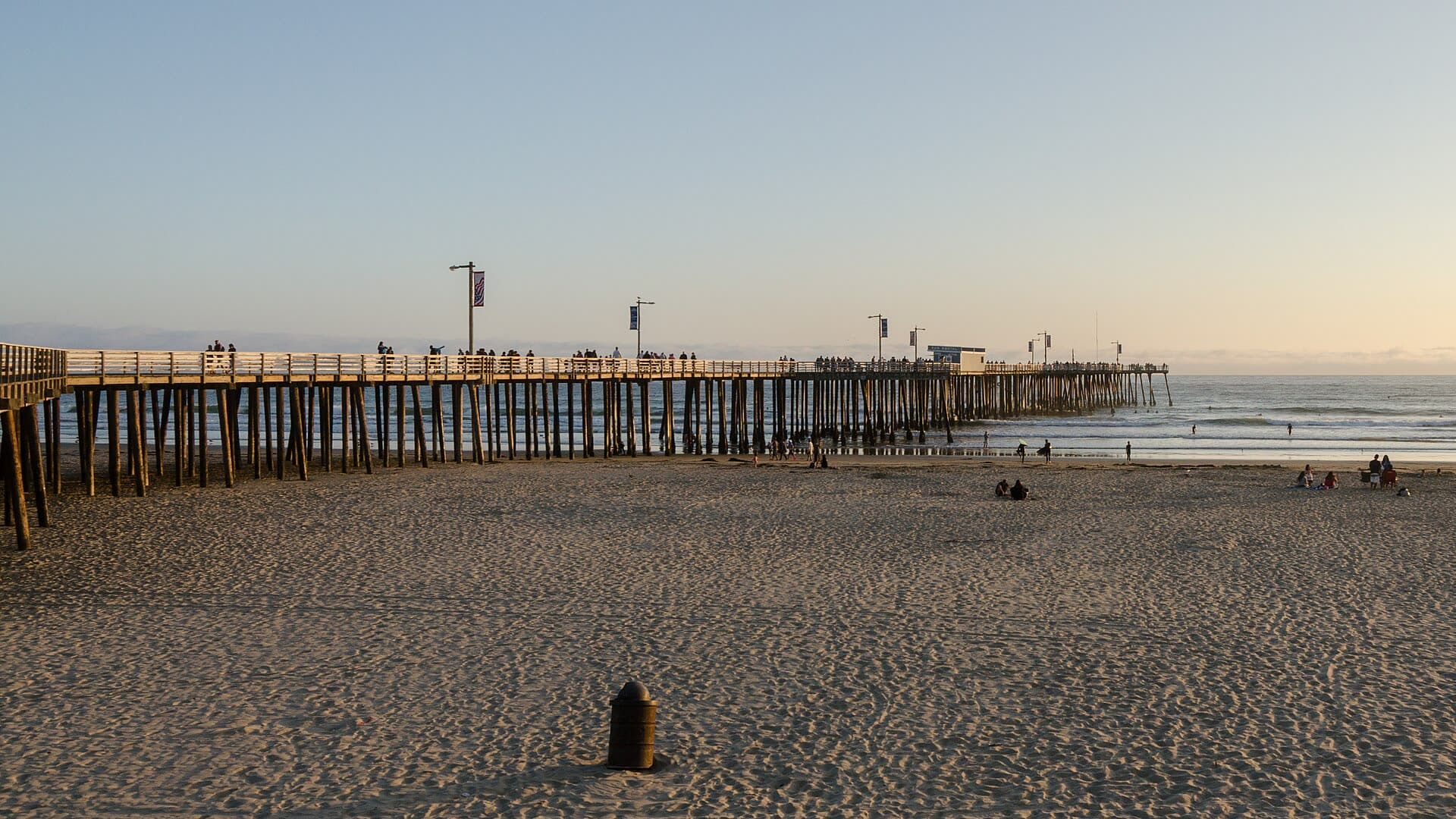 The Pismo Beach Pier stretching out over the surf at sunset, seen from the wide sand north of the pier