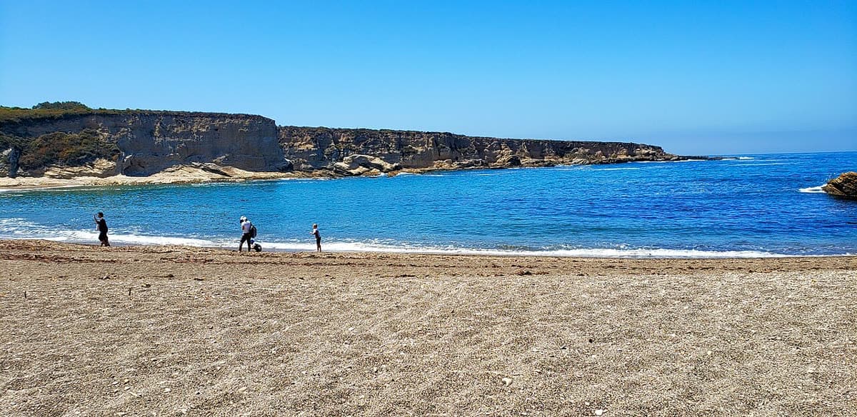 The sandy beach of Spooner's Cove in Montaña de Oro State Park, with blue water and layered cliffs to the south