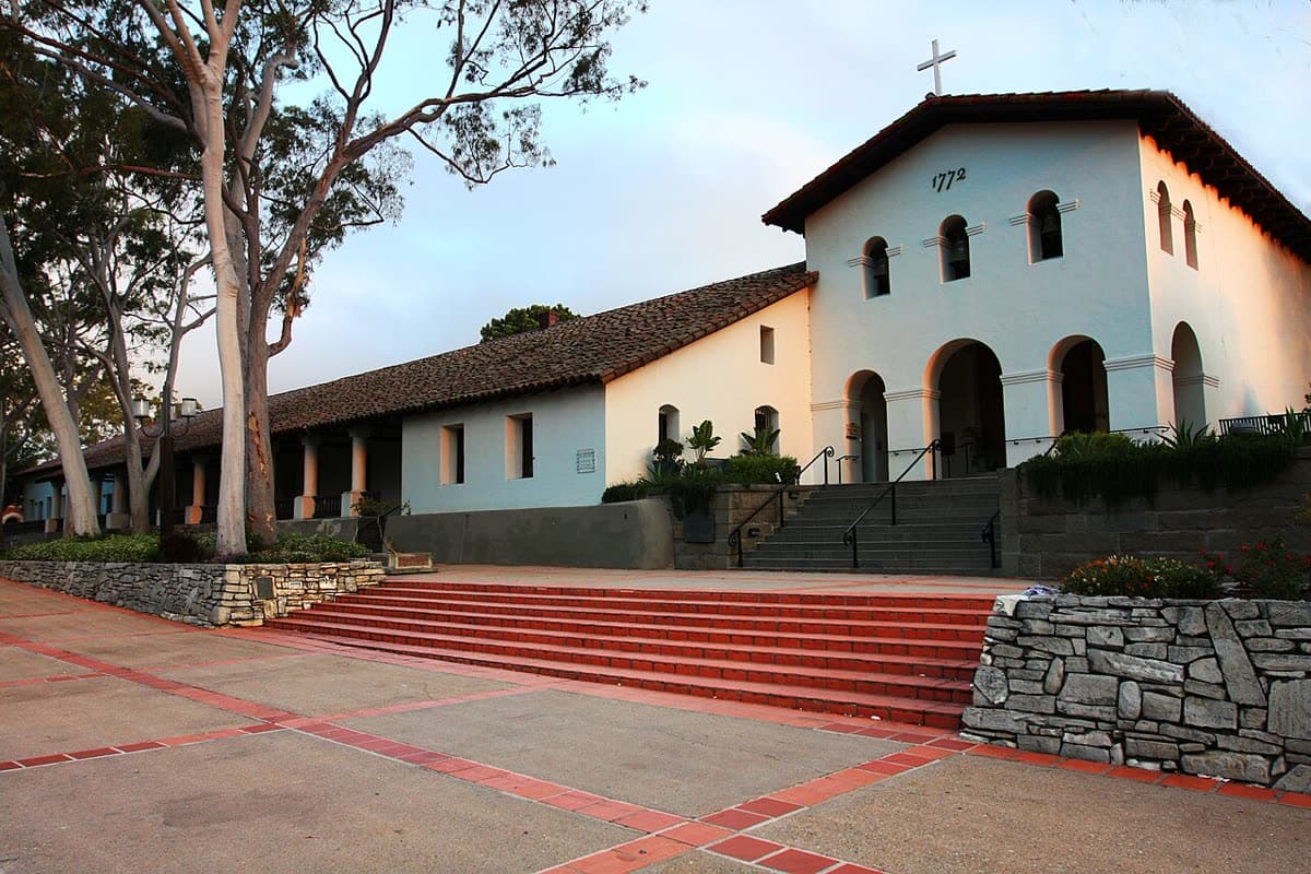 The white facade and bell openings of Mission San Luis Obispo de Tolosa above red steps on Mission Plaza, framed by eucalyptus trees