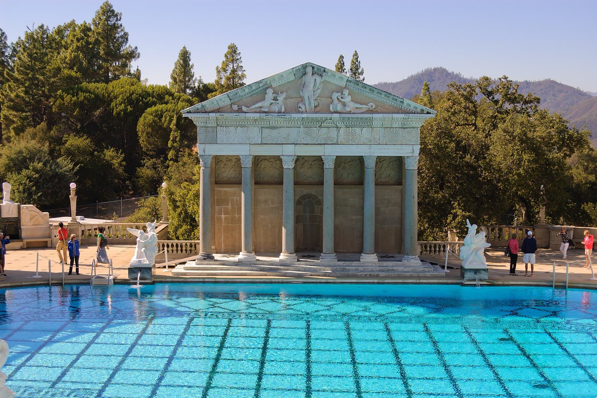 The Neptune Pool at Hearst Castle, its blue-and-white tiled water in front of a white Greco-Roman temple facade and statues, with oaks and hills behind